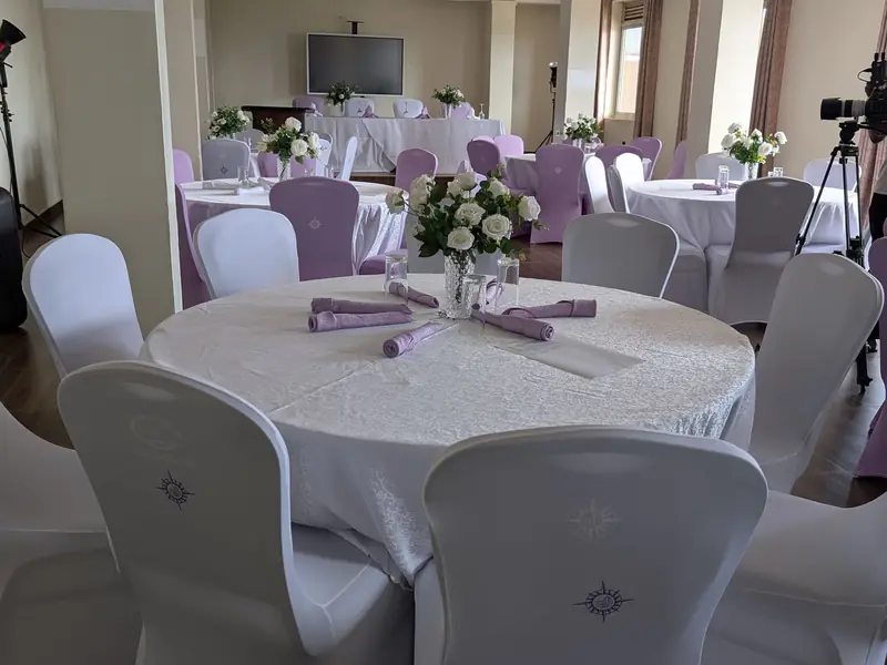 Namirembe Hall laid out banquet-style with dressed round tables and covered chairs