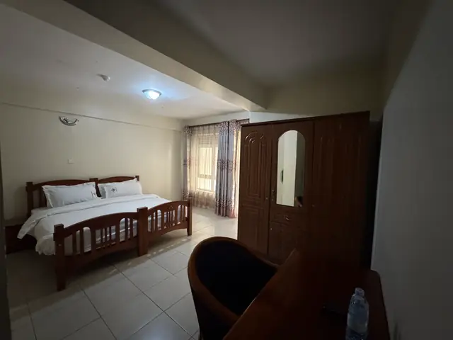 Executive Double Room: bed, wooden wardrobe and armchair beside the window